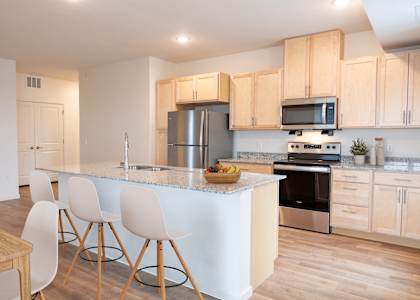 a kitchen with a large island with white chairs and a counter top