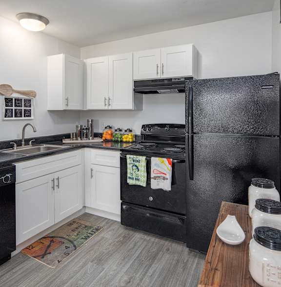 A black refrigerator is in the corner of a kitchen with white cabinets.