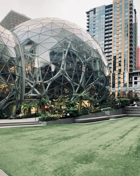 two large spheres in a park in a city with tall buildings