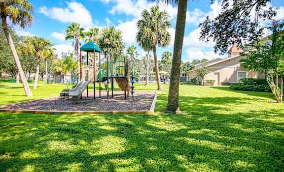 a playground with a slide in the middle of a grassy area with palm trees