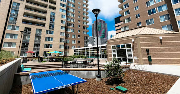A blue table tennis table is in the foreground of a courtyard with a building in the background.