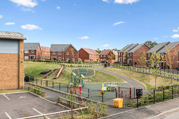 A playground with a slide and a green area in front of a residential area.