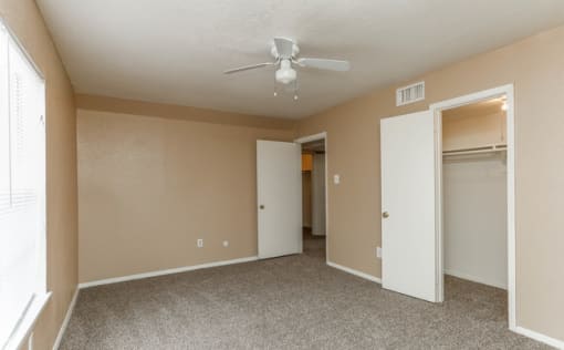 Bedroom with brown walls, brown plush carpeting, spacious closets, and a white ceiling fan.
