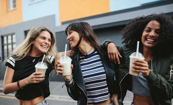 three women walking down the street with drinks in their hands