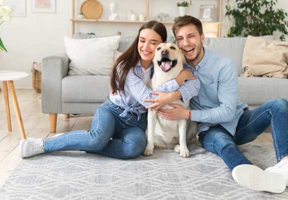 A man and woman are sitting on the floor with a dog between them.