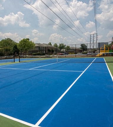 a tennis court with blue and green court surfaces and buildings in the background