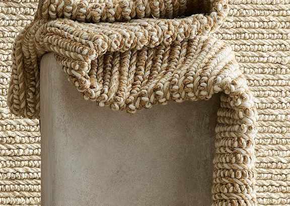 A beige knitted throw is draped over a grey column.