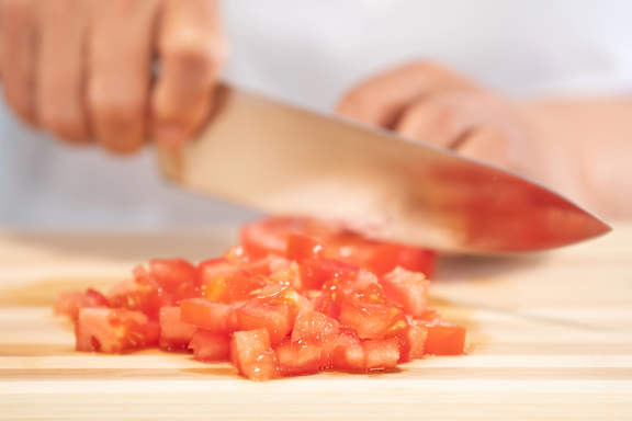 A person cutting a lemon on a wooden cutting board.