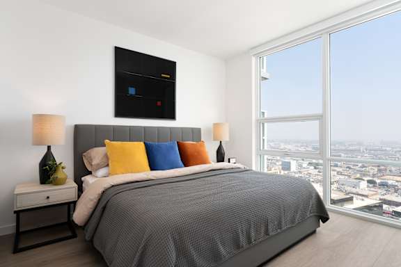 A bedroom with a large bed and a city view through the window. at Olympic + Hill Apartments, Apartments, Los Angeles, CA