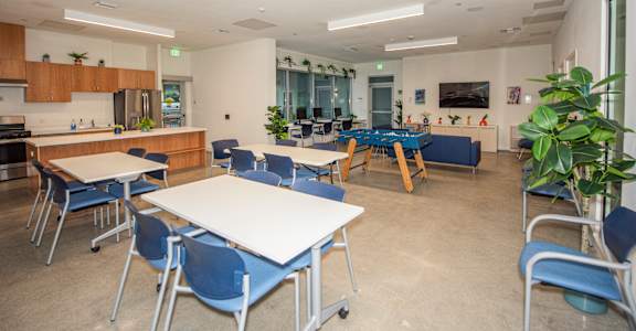 A room with tables and chairs and a kitchen area.