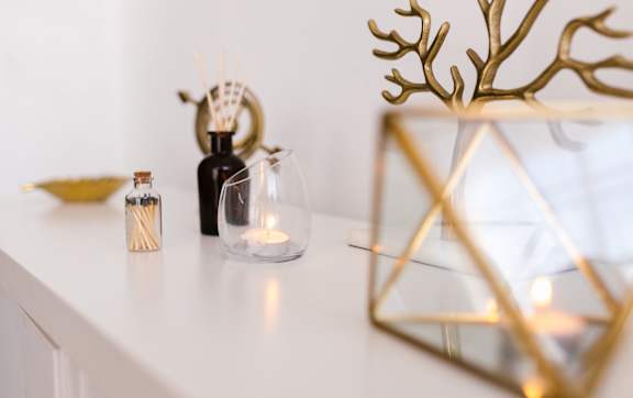 A white shelf with a gold geometric vase and a candle holder with a lit candle.