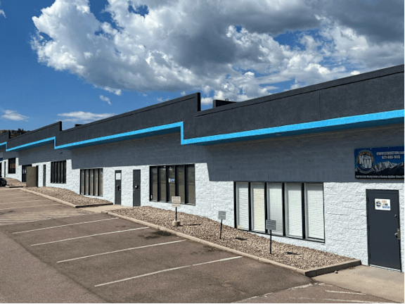 A parking lot in front of a building with a blue line on the roof.
