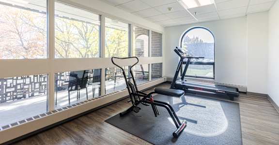 A gym room with a treadmill, exercise bike, and a chair.