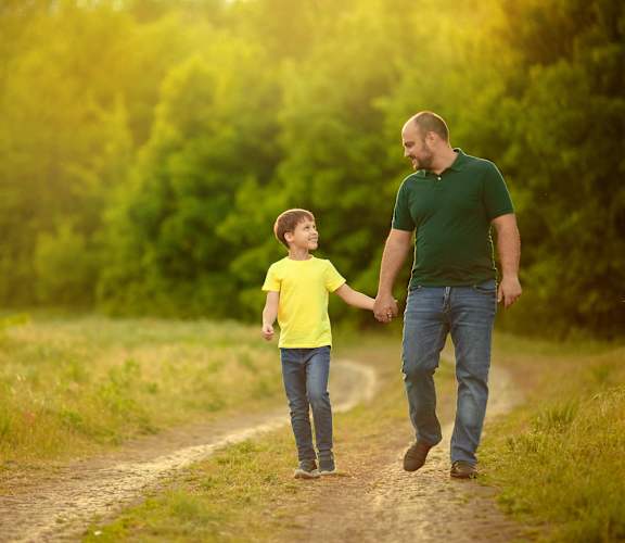 A man and a child are walking hand in hand on a dirt path.
