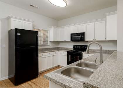 A black refrigerator is in a kitchen with white cabinets and a granite countertop.