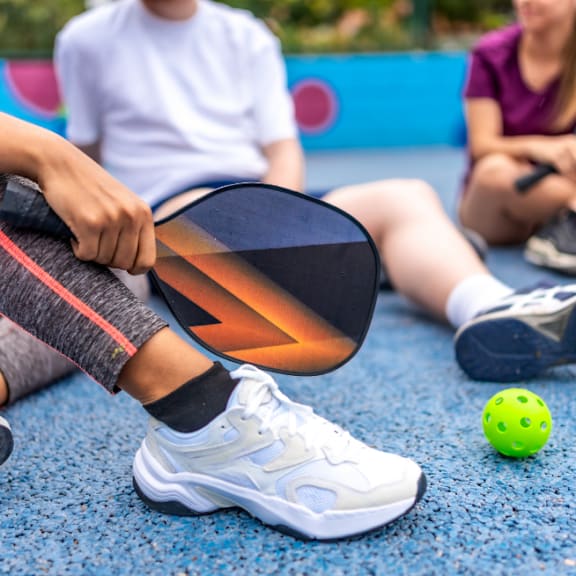 Person Sitting on Ground Holding Pickleball Paddle