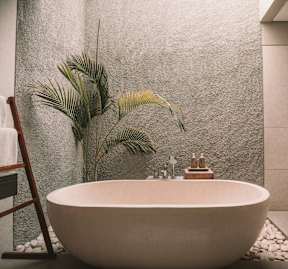 A white freestanding bathtub sits in a bathroom with a plant and a wooden ladder nearby.