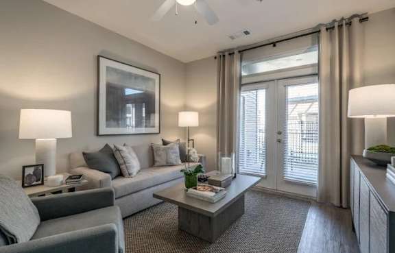 A living room with a grey couch, a grey armchair, a coffee table, and a painting on the wall.