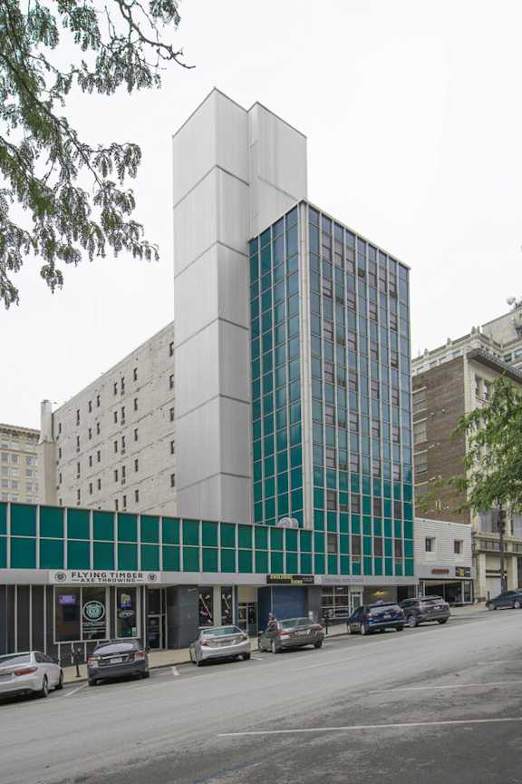 A modern building with a glass facade is situated on a street with cars parked in front.