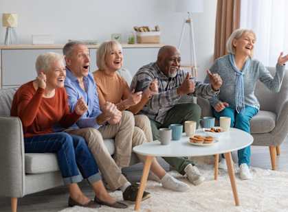 A group of elderly people are sitting on a couch and watching something on a tablet.