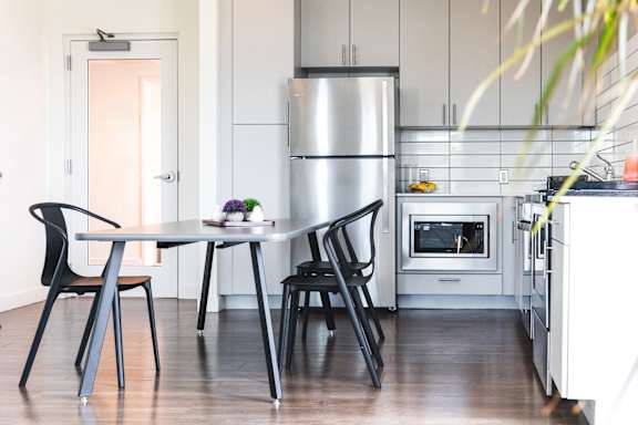 A kitchen with a table and chairs in the foreground and a refrigerator in the background.