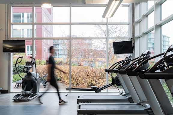 A person is running on a treadmill in a gym with a row of treadmills on the right.