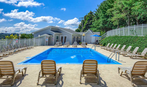 A pool surrounded by chairs and a building in the background.