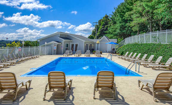 A pool surrounded by chairs and a building in the background.