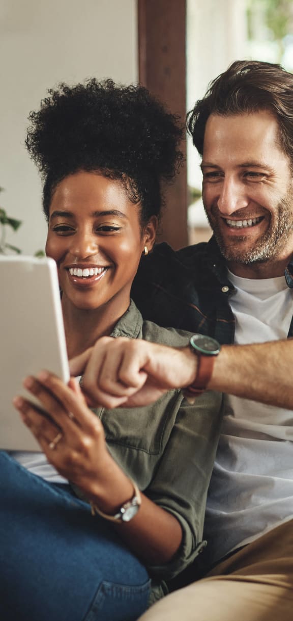 two people sitting on a couch looking at a tablet computer