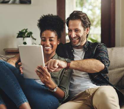 A man and woman are sitting on a couch, looking at a tablet together.