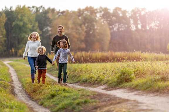 A family of four is walking down a dirt road holding hands.