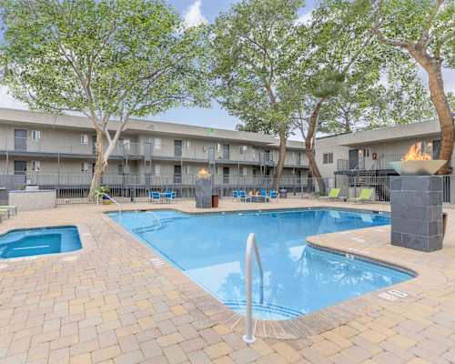A pool surrounded by trees and chairs in front of a building.