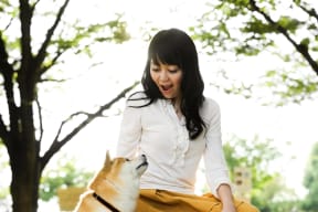 A woman in a white shirt and yellow skirt is sitting on the ground with a brown and white dog. at Bridgwater, Greenwood Village, CO, 80111