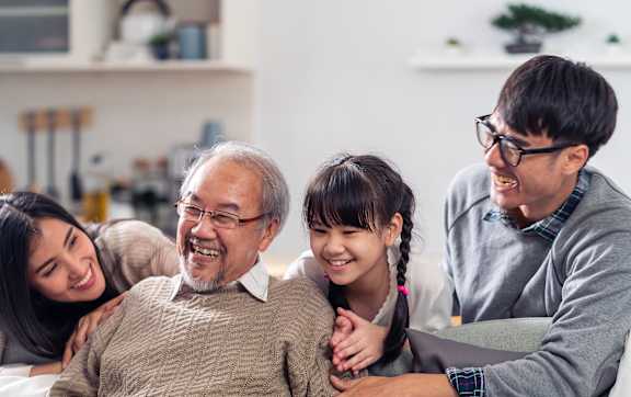 A family of four is sitting closely together on a couch.