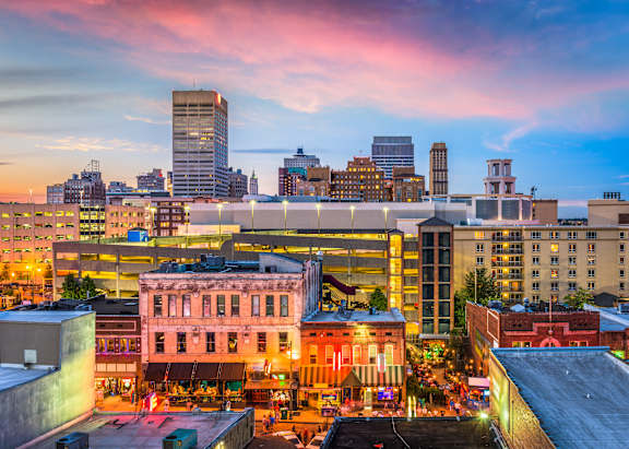 A cityscape at dusk with buildings illuminated and a clear sky.