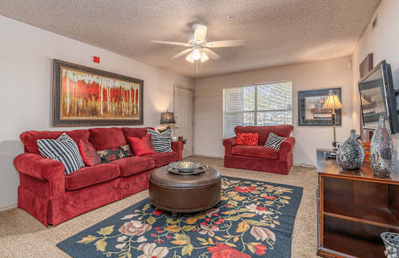 a living room with red couches and a rug and a ceiling fan