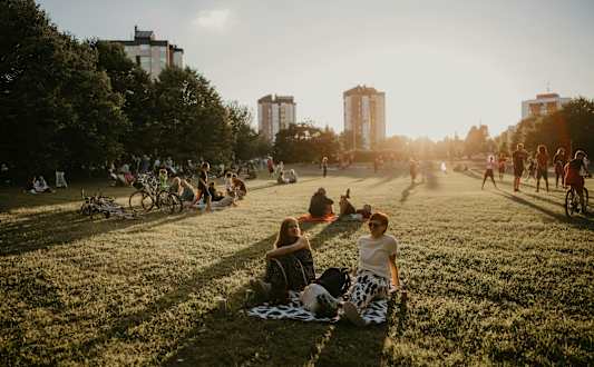 A group of people are sitting on a blanket in a park.