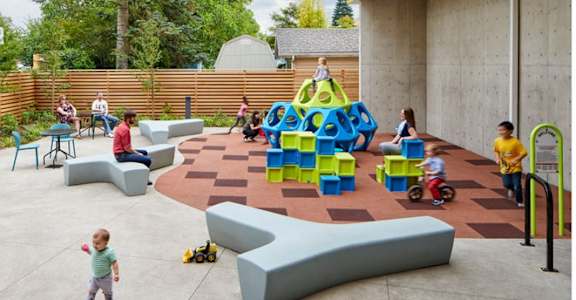 A playground with children playing and a child sitting on a slide.