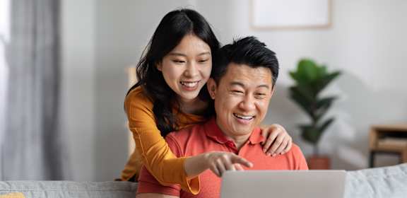 A man and woman are sitting on a couch with a laptop.