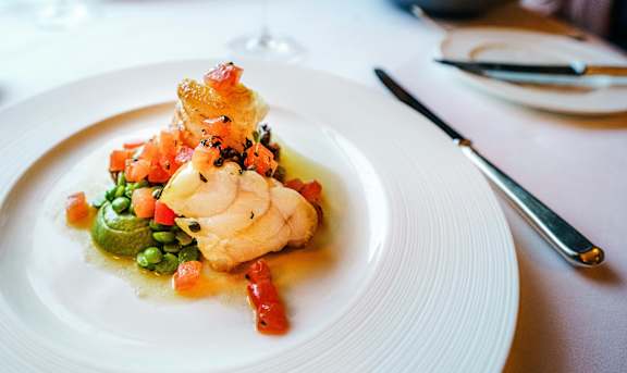 A white plate with a piece of fish and vegetables on it.
