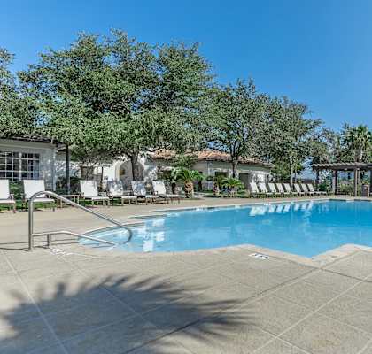A large swimming pool surrounded by trees and lounge chairs.