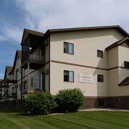 Fargo, ND Village Park Apartments. An exterior view of a large apartment building with a grassy area in front of it
