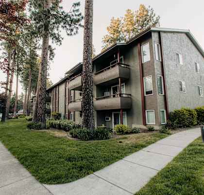 the side of a building with a sidewalk and trees