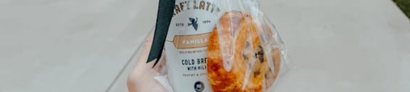 A person is holding a bag of doughnuts in front of a house.