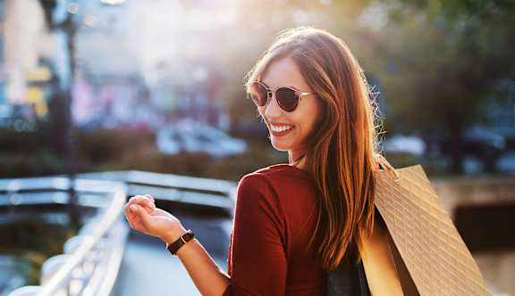 A woman with sunglasses and a red top is holding a brown paper bag.