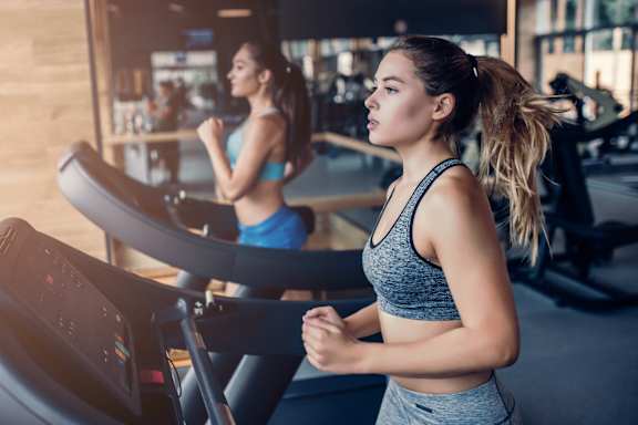 A woman is running on a treadmill in a gym.
