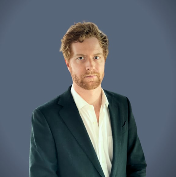 A man with a beard wearing a green jacket and white shirt.