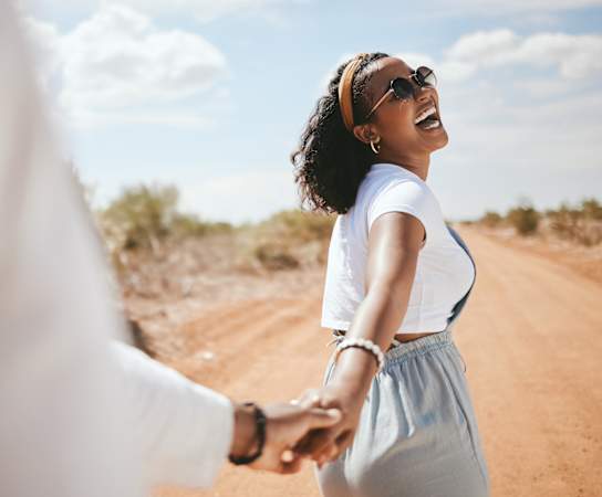 A woman is holding hands with a man on a dirt road.