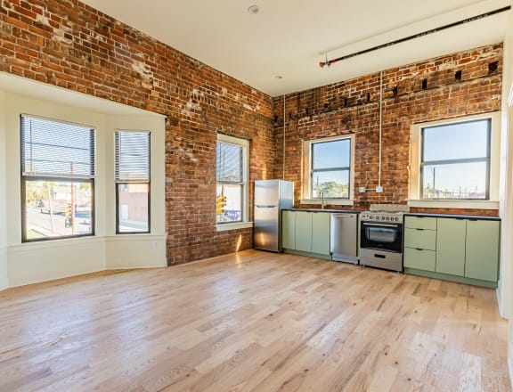 an open concept living room and kitchen with exposed brick walls and hardwood floors