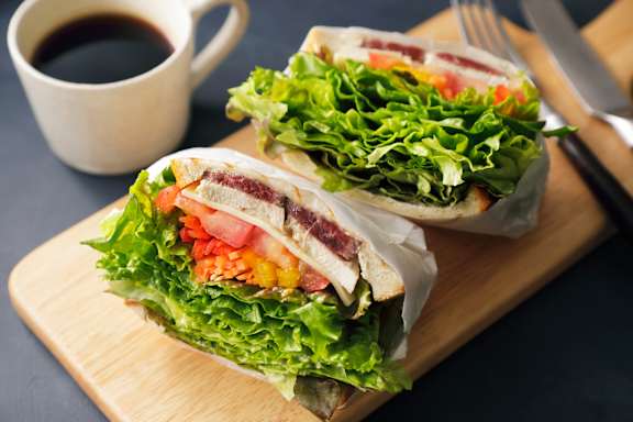 A sandwich with lettuce, tomato, and other vegetables is cut in half and served on a wooden board with a cup of coffee at Hampton Plaza Apartments, Towson, MD, 21286